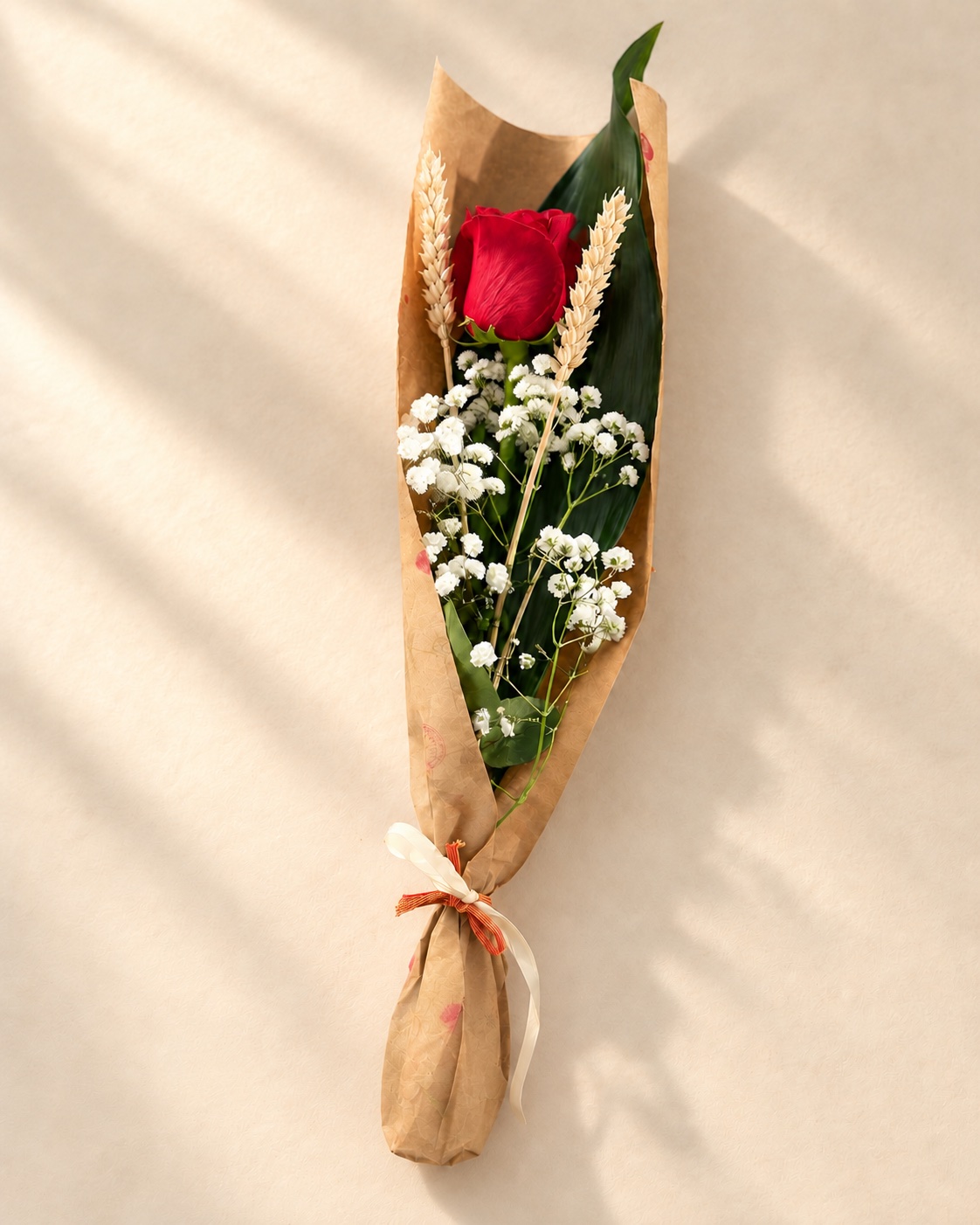 Rosa vermella amb dues espigues i flors blanques, embolicada en paper kraft.